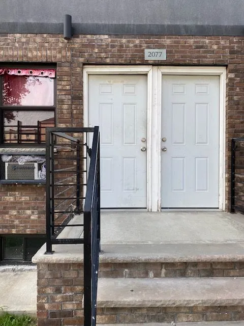 Brick building entrance at 2077 with white double doors and a black metal handrail