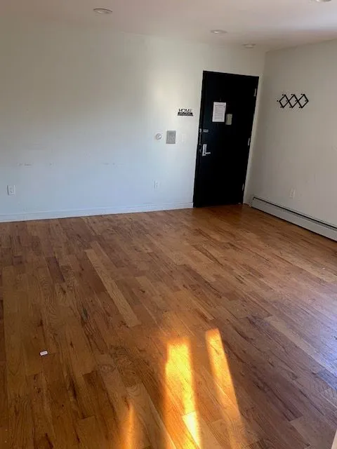 Empty Caesar Pl 2L room with polished hardwood floors, white walls, and a black entry door