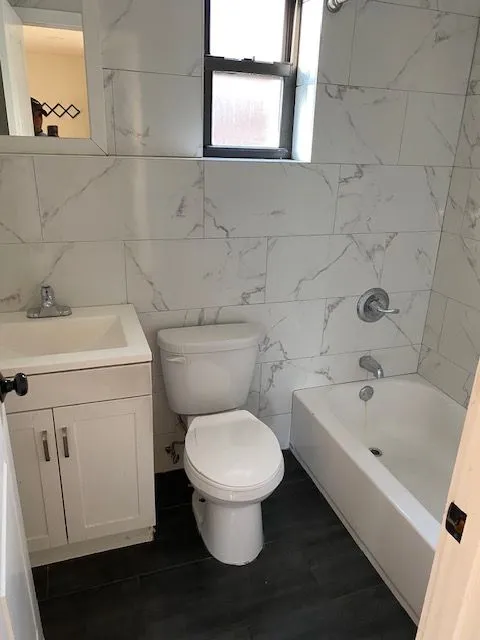 Caesar Pl 2L bathroom with a white vanity, toilet, bathtub, and marble-look wall tile