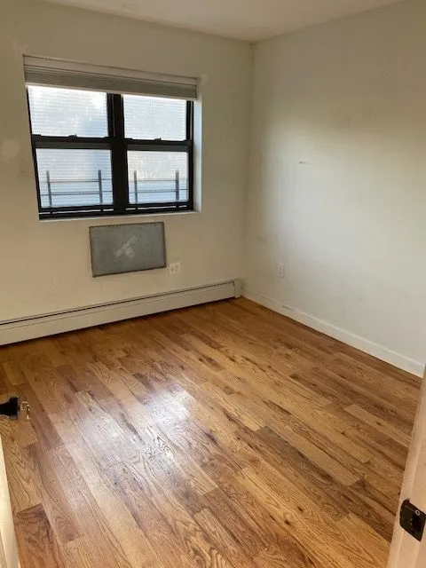 Empty Caesar Pl 2L room with hardwood floors, a wide window, and a baseboard heater