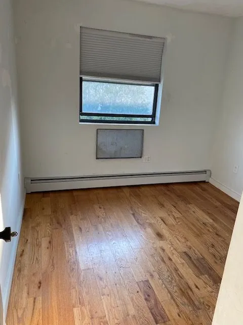 Empty Caesar Pl 2L room with hardwood floors, a window, and a baseboard heater