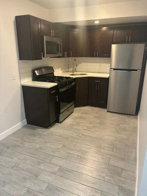 Yonkers Ave #1 kitchen with dark cabinets, stainless steel appliances, and a tiled backsplash
