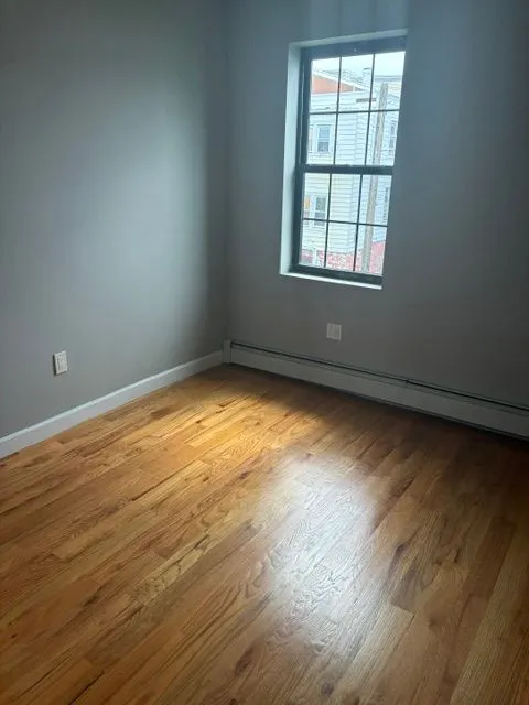 Sunlit room with hardwood floors, a window, and radiator