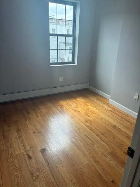 Empty hardwood-floored room with a tall window